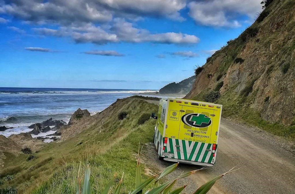 A Wellington Free Ambulance on the side of the road by a coastline.