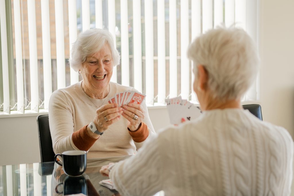 Two elderly friends play cards while they wear Freedom Medical Alarms.