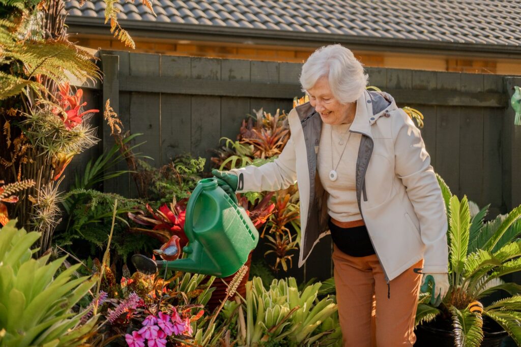 An elderly woman waters her garden.