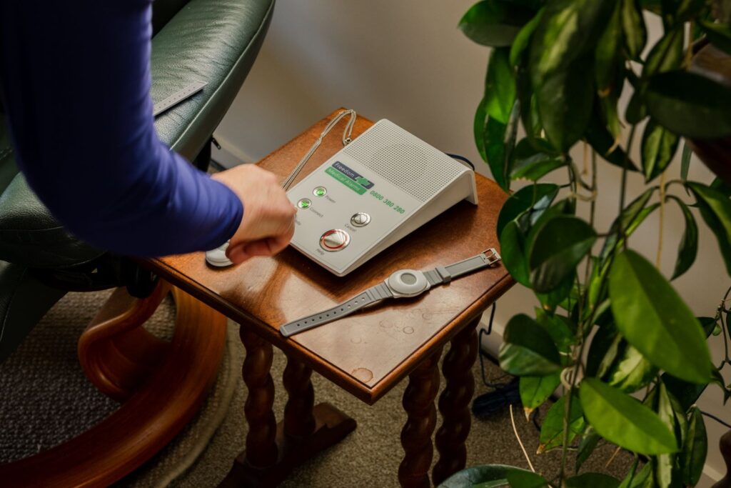 A hand reaches towards various Freedom Medical Alarms devices.