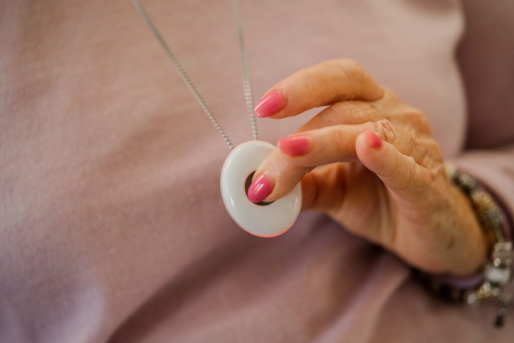 An elderly woman presses the button on a medical alarm neck pendant.