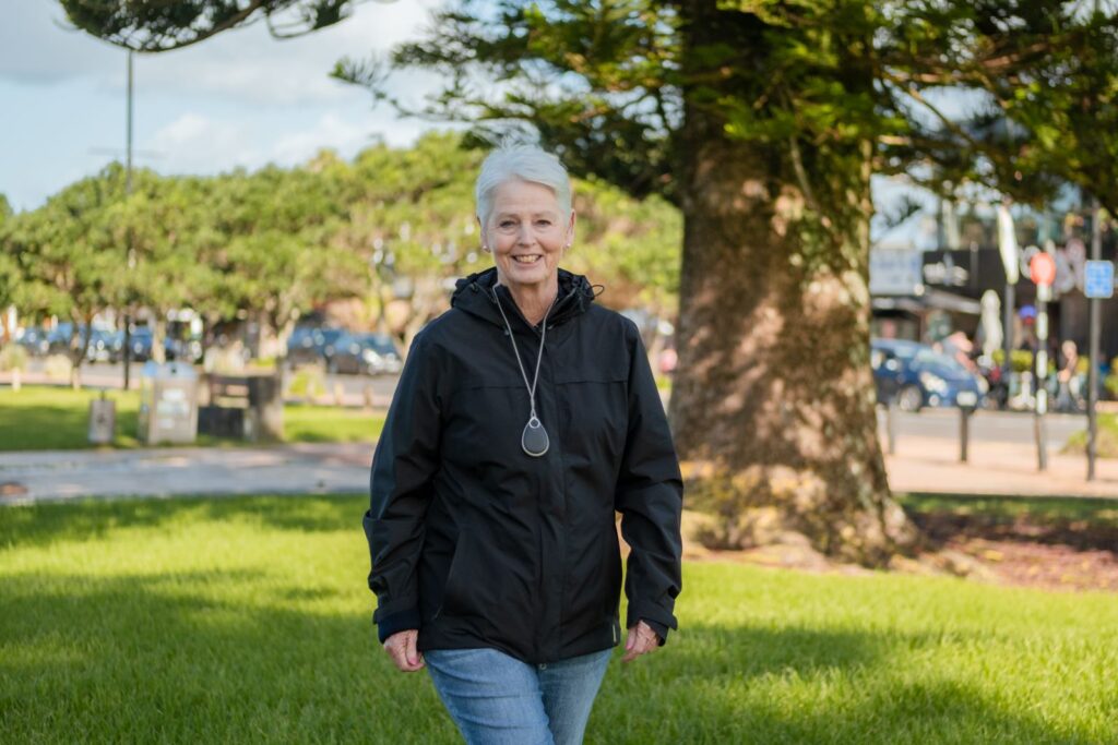 An elderly woman wearing a GO Pendant medical alarm walks in the park.